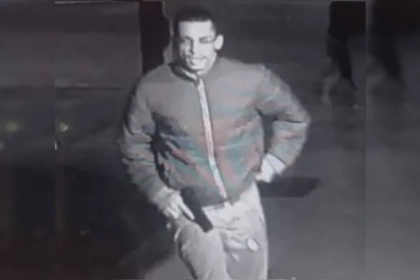 Foto em preto e branco de criminoso com arma roubada de policial militar, após agressão da vítima