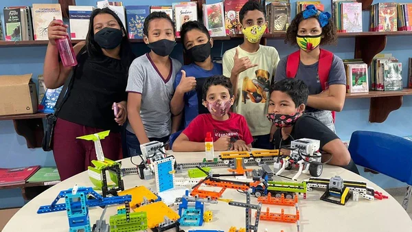 crianças reunidas atrás de uma mesa com objetos coloridos
