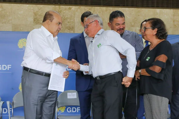 Homem careca de roupa social apertando a mão de homem, também de roupa social, de cabelos grisalhos