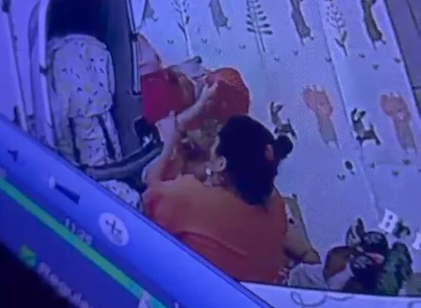 Foto colorida retirada de câmera de segurança que mostra babá praticando maus-tratos contra bebê e criança - Metrópoles