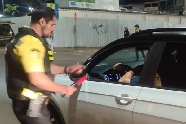 Imagem colorida de agente do Detran conversando com motorista em carro branco