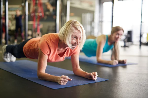 Mulher loira de meia idade e ativa fezendo exercícios para o abdômen, uma prancha no tapete durante treino no centro de fitness - exercício