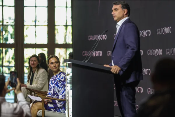 Imagem colorida de Flávio Bolsonaro acompanhado da esposa em evento para mulheres - Metrópoles