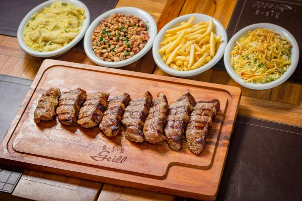 Foto colorida de uma tábua com carne fatiada e porções de arroz, farofa, batata frita e feijão tropeiro - Metrópoles