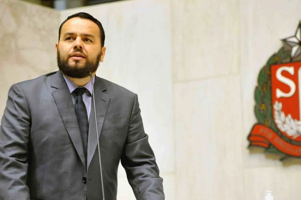 Imagem colorida mostra Gil Diniz, homem com barba preta, vestindo terno, apoiado sobre um púlpito de fundo branco; ele é novo integrante do conselho de direitos humanos - Metrópoles