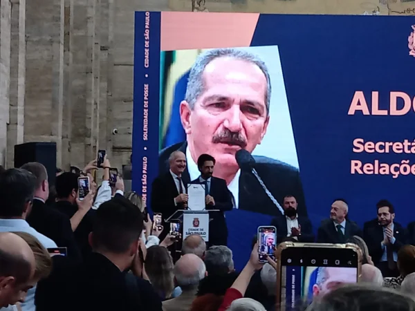 Imagem colorida mostra Aldo Rebelo e Ricardo Nunes mostrando documento de posse de Algo em um palco da prefeitura repleto de pessoas - Metrópoles