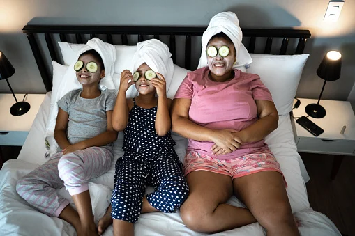 Três mulheres deitadas na cama com toalha na cabeça e pepino nos olhos