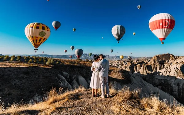 Na foto, um casal em uma montanha com vários balões voando