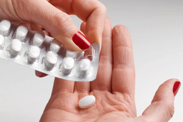 Mão feminina com esmalte vermelho nas unhas colocando medicamento - Metrópoles
