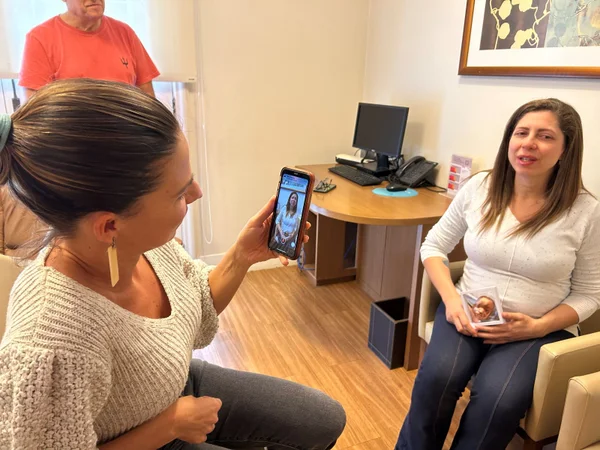 Imagem mostra mulher com celular na mão filmando uma mulher grávida sentada em poltrona - Metrópoles