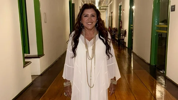 A atriz Regina Casé posa dentro de uma casa histórica usando um vestido branco - Metrópoles