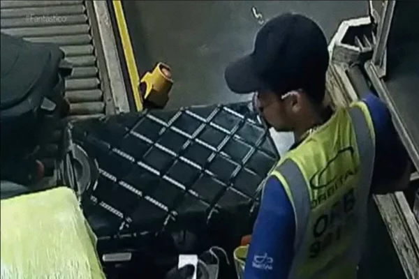 Homem com colete refletor amarelo obsrva bagagem em esteira de terminal de cargas - Metrópoles