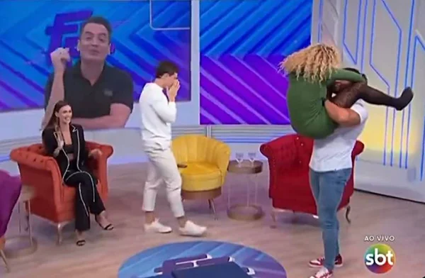 foto colorida de mulher no colo de homem enquanto outras pessoas observam - metrópoles