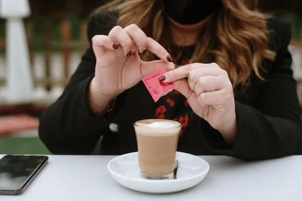 Pessoa colocando adoçante em copo com café- Metrópoles
