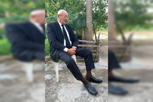 Foto colorida de homem idoso com terno sentado em banco