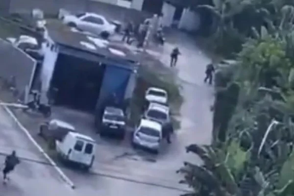 Imagem colorida mostra policiais militares, longe, correndo em viela de morro, perto de área de mata - Metrópoles