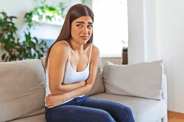 Foto colorida de mulher com mão na barriga, aparentemente com flatulências