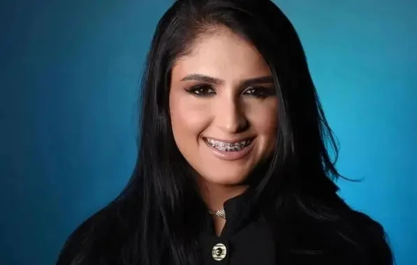 Foto mostra mulher morena de aparelho e maquiada sorrindo para a câmera