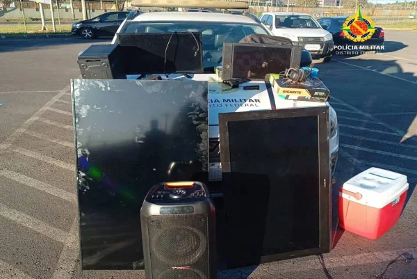 Foto colorida tirada de dia de vários eletrônicos amontoados em frente a carro da policia militar
