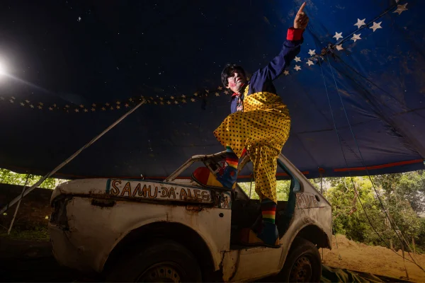 Foto colorida mostra um palhaço sobre um carro velho debaixo de uma lona de circo. O palhaço Juquinha é um dos personagens entrevistados em matéria do Metrópoles sobre circos