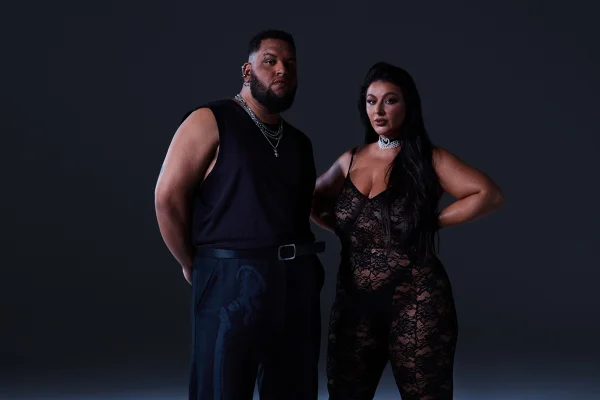 Homem usa look de alfaiataria com colete e mulher usa macacão de renda preto - Metrópoles