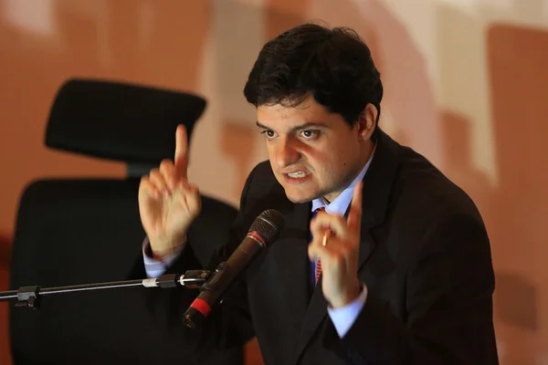 Homem de terno, com os dedos para o alto, falando em microfone