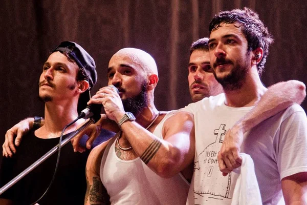 Foto da banda Forfun. São quatro homens brancos abraçados em um palco - Metrópoles