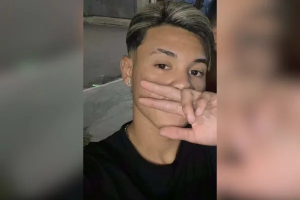Imagem colorida mostra adolescente branco com cabelos escuros com mecha descolorida. Ele olha para a câmera e cobre parte do rosto fazendo um sinal com três dedos com a mão direita - Metrópoles
