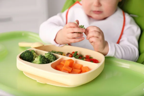 Bebê comendo comida na cadeira alta, close-up. Bebê alimentação saudável. Metrópoles