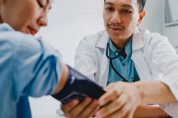 Close de um médico asiático maduro medindo a pressão arterial (alta ou baixa) de uma paciente em uma clínica de saúde. Conceito de assistência médica. Médico mede a pressão cardíaca de paciente coração diabetes infarto pressão alta