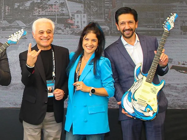 Imagem colorida de Ricardo Nunes, prefeito de SP, de terno cinza e camisa branca, à direita, segurando uma guitarra azul - Metrópoles