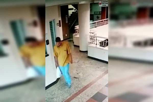 No frame, homem negro, de estatura média e roupas folgadas caminha em hall de prédio com sacola plástica na mão. Ele é acusado de roubar prostitutas no Distrito Federal - Metrópoles