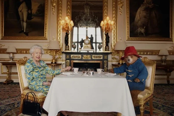 Foto colorida. Rainha Elizabeth e urso Paddington