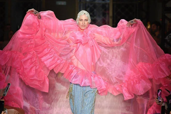 Na passarela, modelo abre os braços estendendo o tecido rosa transparente do look - Metrópoles