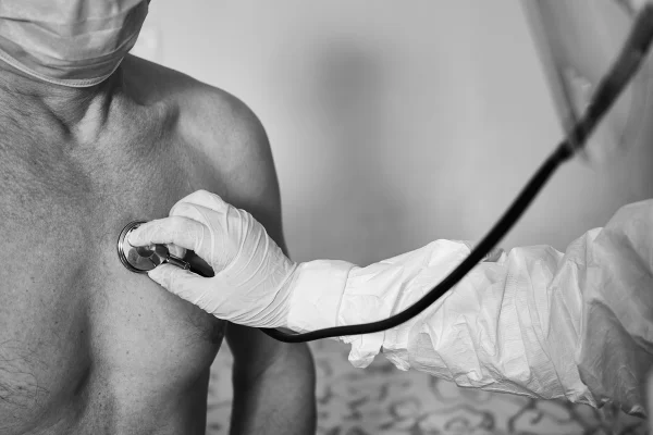 Foto em preto e branco de médico com estetoscópio ouvindo o coração de um homem - Metrópoles