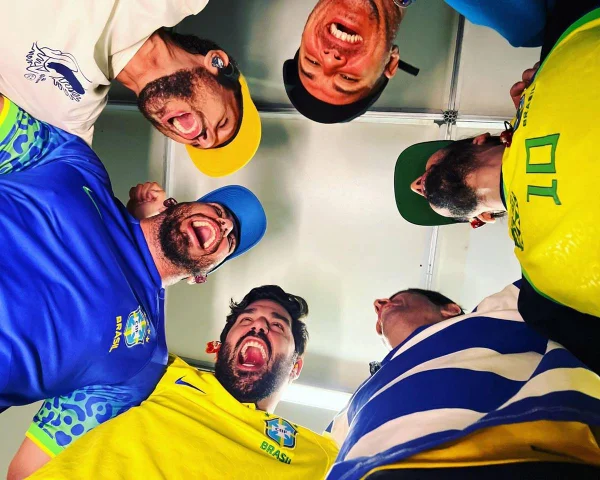 foto tirada de baixo para cima com seis homens rindo vestidos de blusas do brasil - metrópoles