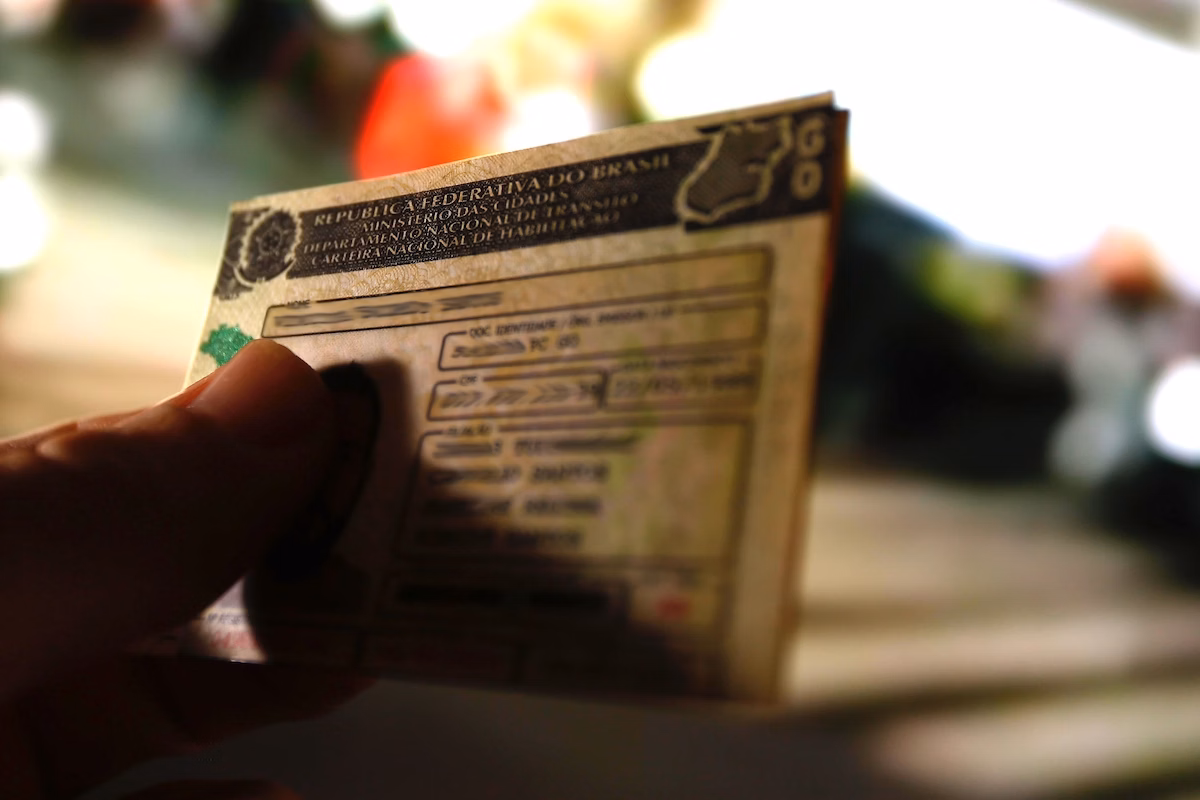 Imagem colorida de uma mão segurando uma carteira nacional de habilitação. Os dados estão borrados