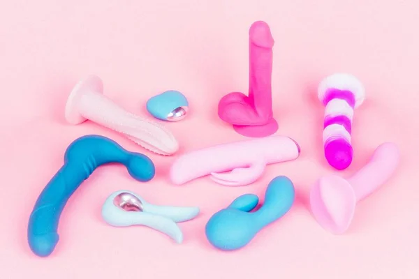 Vibradores em forma de pênis de cores e formatos diferentes espalhados em fundo rosa - Metrópoles