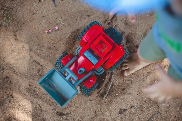 Fotografia colorida mostrando caminhão de brinquedo aos pés de criança em parquinho de areia-Metrópoles