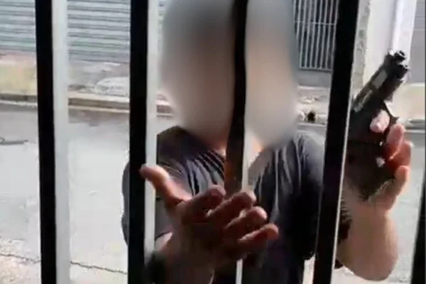 Imagem colorida de menino com arma de brinquedo atrás de portão de uma casa - Metrópoles