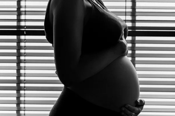 Foto em preto e branco de mulher grávida com as duas mãos na barriga - Metrópoles.