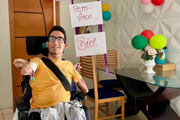foto colorida de jovem com paralisia cerebral com cartaz ao lado escrito bem vindo - Metrópoles.