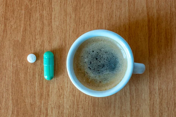 Foto colorida - Xícara de café com cápsulas de suplementos