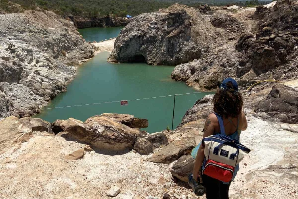 Adventure Park Cristalina. Na foto uma mulher de costa com uma mochila olhando para um lago na cor azul esverdeado - Metrópoles