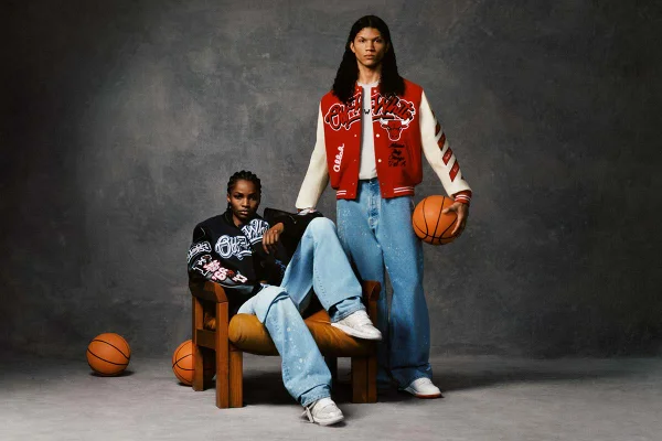 Campanha de divulgação da coleção de roupas da marca Off-White com o time de basquete Chicago Bulls. Na imagem, é possível ver uma mulher negra e um homem pardo, ambos jovens, posando para foto em um fundo cinza com bolas de basquete. Ambos usam calças jeans e tênis esportivos, mas ela usa uma jaqueta preta e ele uma vermelha. - Metrópoles