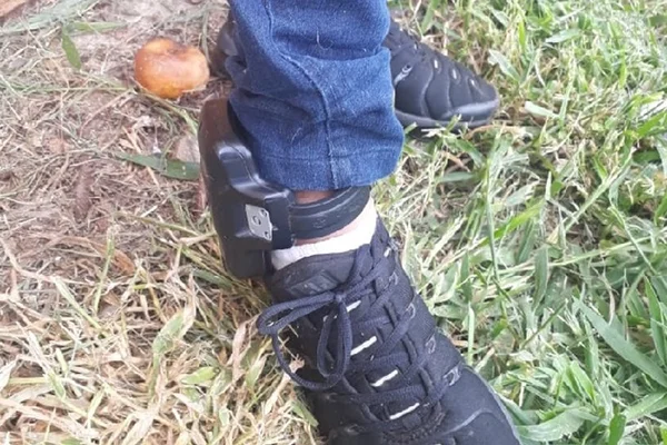 Foto colorida de tornozeleira em pé de pessoa no mato