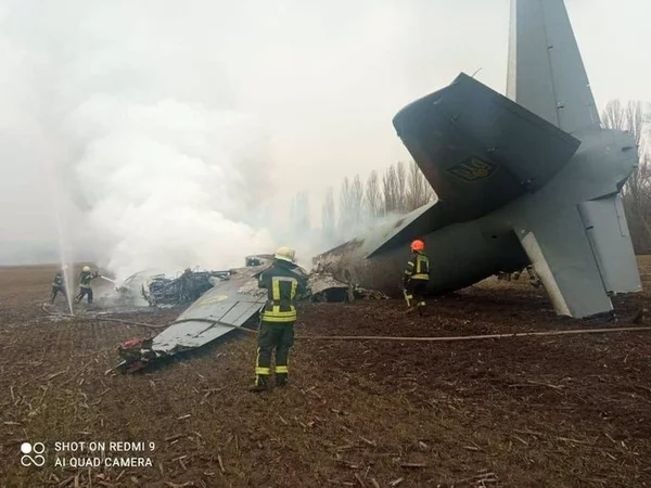 Avião ucraniano cai com 14 militares a bordo. O avião aparece destruído no chão, no que parece ser uma floresta, soltando muita fumaça e com bombeiros em volta - Metrópoles