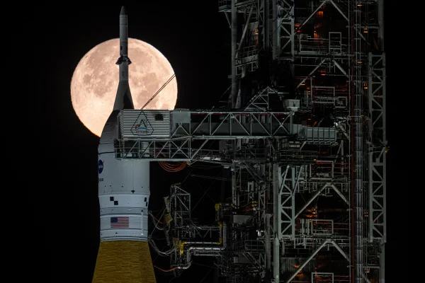 Imagem colorida mostra foguete SLS da Artemis II com a Lua ao fundo - Metrópoles