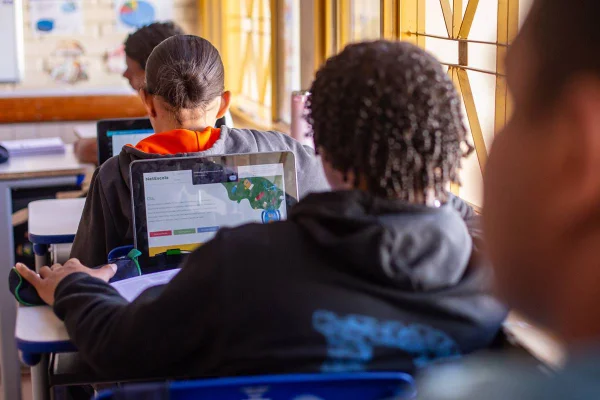 Imagem de adolescentes de costas, sentados em sala de aula