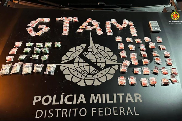 Foto colorida de porção de cocaína em saquinhos em cima de capô de carro de Polícia